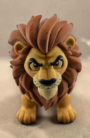 Pohyblivá 3D tištěná figurka lva se žlutým tělem a hnědou hřívou na pískovém podkladu.